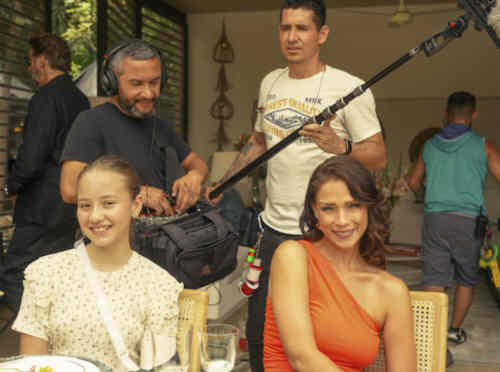 Carolina Miranda mit schulterfreiem orangenem Kleid am Set